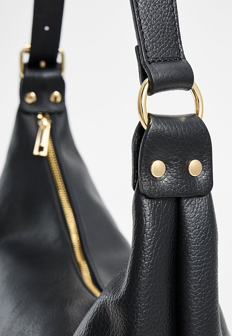 Sac en cuir noir avec une surface texturée, matériel doré et détail en zip. Dispose de anses robustes et de clous décoratifs.