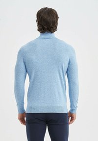 Pull bleu clair avec un col haut, des poignets et un ourlet côtelés. Texture lisse ; design ajusté qui met en valeur les épaules et le dos.