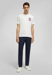 Witte katoen t-shirt met een meerkleurige grafiek met zwarte, rode en marineblauwe strepen. Gecombineerd met marineblauwe broek en witte sneakers.