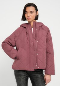 Πουπουλένιο, με κουκούλα μπουφάν σε απαλό ροζ χρώμα με κλείσιμο με φερμουάρ και κουμπιά. Διαθέτει πλαϊνές τσέπες και ελαφρώς κομψό κόψιμο.