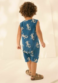 Vestido azul sin mangas con patrones de lagarto, textura suave y un ajuste relajado, combinado con sandalias marrones con tiras ajustables.