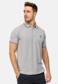 Šedé polo tričko s límečkem, který má červené a námořnické akcenty, krátké rukávy a vyšívané logo na hrudi. Směs bavlny.