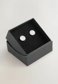 Silver-tone stud earrings with a smooth white circular surface, presented in a black, hinged gift box lined with black fabric.