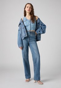 Tenue en denim comprenant une veste croppée bleu clair, un top assorti et un jean taille haute à jambes larges avec une coupe classique. Texture lisse, sans motifs.