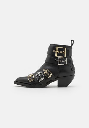 Černá kožená kotníková bota s špičatou špičkou, s několika pásky ozdobenými zlatými a stříbrnými sponami. Design na blokovém podpatku.