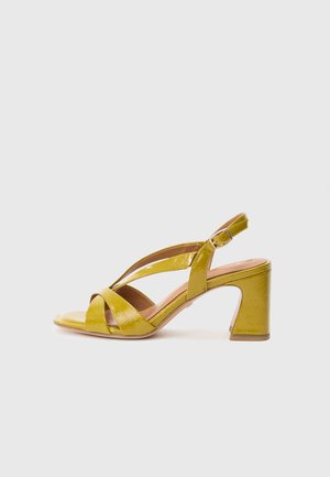 Sandale en cuir verni jaune avec brides croisées et boucle à la cheville, dotée d'un talon bloc et d'une finition lisse et brillante.