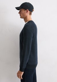 Granatowy sweter dziany z okrągłym dekoltem i długimi rękawami, o fakturowanym materiale, zestawiony z czarną, dopasowaną czapką.