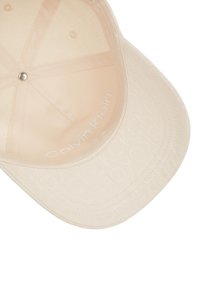 Cappello beige con visiera curva, tessuto testurizzato con logo Calvin Klein all'interno. Design elegante con hardware minimale e senza motivi visibili.