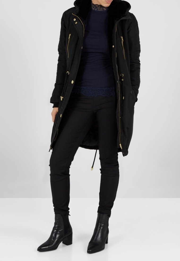 Černý dlouhý kabát se zlatými zipy a stahovacím šňůrkem, s kapucí z umělé kožešiny. Nošený přes námořnicky modrý top a černé přiléhavé kalhoty, doplněný kotníkovými botami.