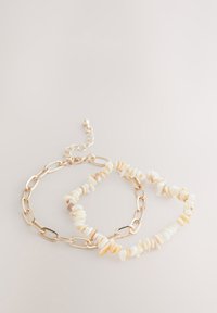 Gold chain bracelet featuring irregular white and beige shell pieces, with a textured surface and a lobster clasp for adjustable fit.