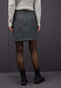 Svart och vit skir med Chevron-mönster, med en figurnära design, texturerad tyg och längd ovanför knäna. Stylad med svarta ankelstövlar.