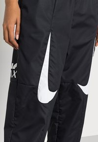 Svarta träningsbyxor med vitt Nike-logotyp och swoosh-accenter. Tillverkade av slätt, lättviktigt tyg med en tapered passform.