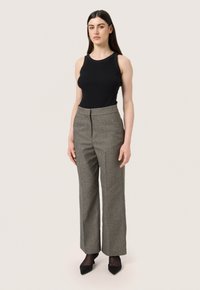 Top aderente nero a coste abbinato a pantaloni grigi a quadri a vita alta. I pantaloni presentano una vestibilità sartoriale e un taglio dritto. Scarpe nere con tacco.