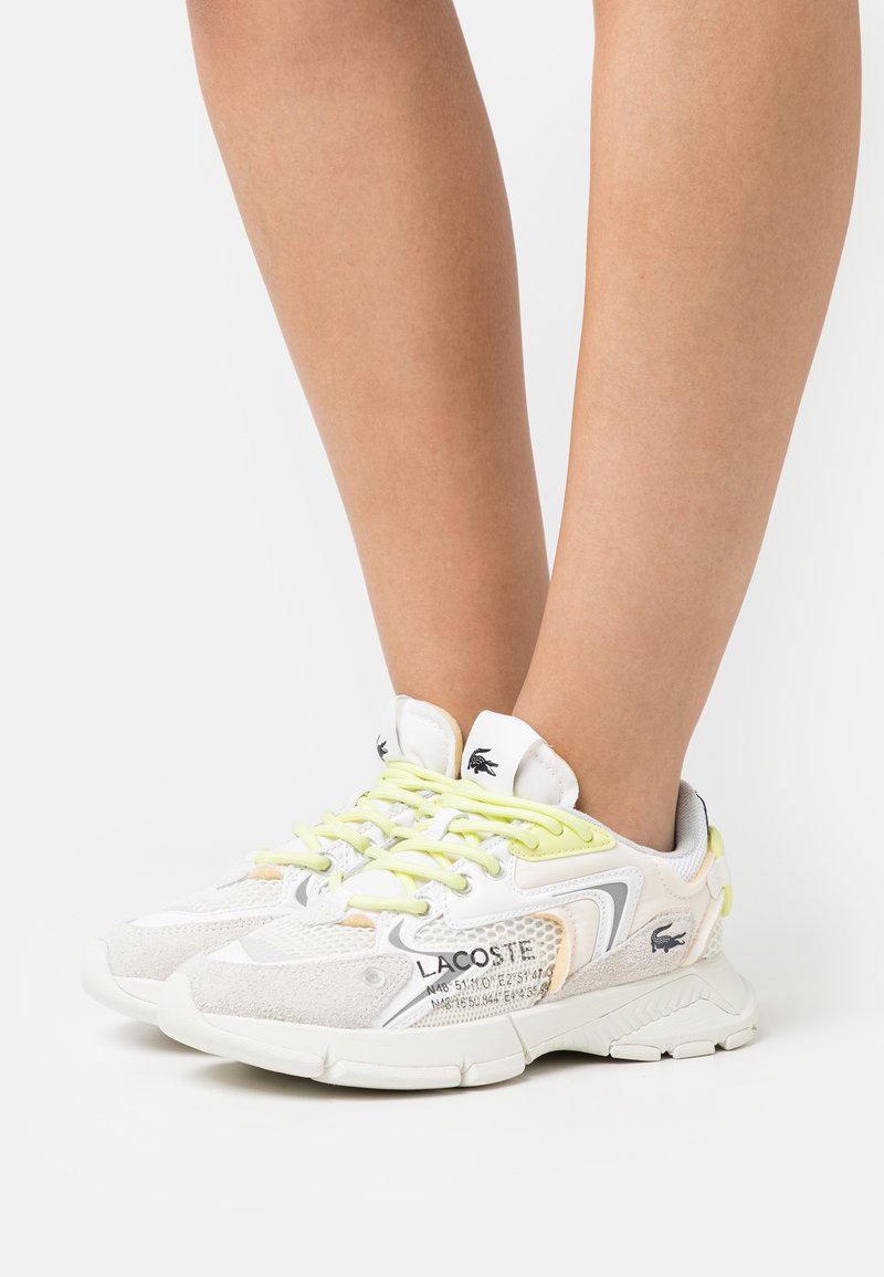 Lacoste sneakers with a mixed material design in white and light gray. Features yellow laces, textured accents, and logo detail on the side.