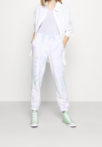 Joggers de tie-dye en colores pastel, con cintura y puños elásticos, combinados con una camiseta blanca y zapatillas altas verdes.