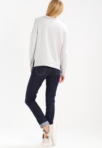 Sudadera gris claro de mangas largas, corte relajado y cuello redondo, combinada con jeans de mezclilla oscuros y zapatillas blancas.