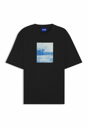 T-shirt en coton noir avec un imprimé graphique bleu représentant un paysage marin avec une jetée et des palmiers, centré sur le devant.