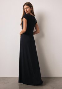 Fekete maxi ruha rövid ujjakkal, testhezálló felsőrésszel és bővülő szoknyával. Fodorral díszített szegéllyel és sima, rugalmas anyaggal.
