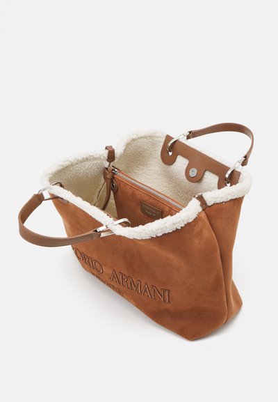 Borsa tote in suede marrone con un morbido rivestimento bianco, hardware argentato e due manici in pelle marrone. Presenta una tasca interna con zip.