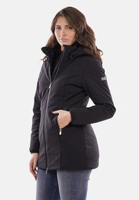 Giacca nera impermeabile con cappuccio, zip frontale, polsini elasticizzati e tasche laterali. Tessuto liscio e design aderente per calore e comfort.