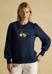 Jūras spēku krekls no kokvilnas ar pūšamām piedurknēm, ar izšūtiem zvaniņiem un dižkoku, papildināts ar tekstu "DING DONG" virs un zem tā.