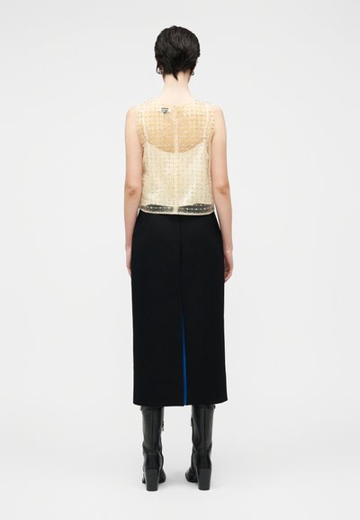 Przezroczysta złota bluzka z koralikami nałożona na czarną dopasowaną spódnicę z niebieskim rozcięciem, zestawiona z czarnymi kozakami za kolano.