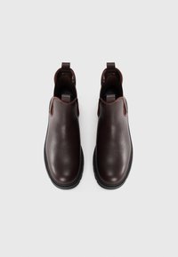 Botas tobilleras de cuero marrón con paneles laterales elásticos, puntera redondeada y un acabado texturizado. Suela de goma negra resistente y tiradores para facilitar su uso.