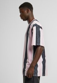 Striped t-shirt featuring vertical black, light pink, and white stripes. Made of cotton with a relaxed fit and short sleeves.