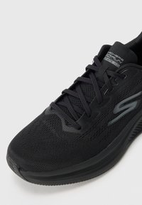 Baskets de sport noires avec un dessus en mesh respirant, fermeture à lacets, semelle rembourrée et semelle extérieure en caoutchouc lisse pour une traction.