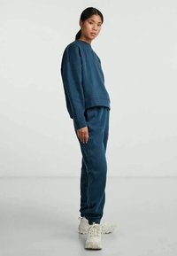 Hanorac bleumarin și pantaloni de trening asortați, confecționați dintr-un material moale, având o croială lejeră și mansete ribbate, asortați cu adidași albi masivi.