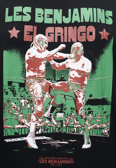 Δύο παλαιστές με μάσκες μέσα σε ρινγκ, ο ένας κλοτσάει και ο άλλος αποκρούει, με το κείμενο «LES BENJAMINS EL GRINGO» από πάνω.