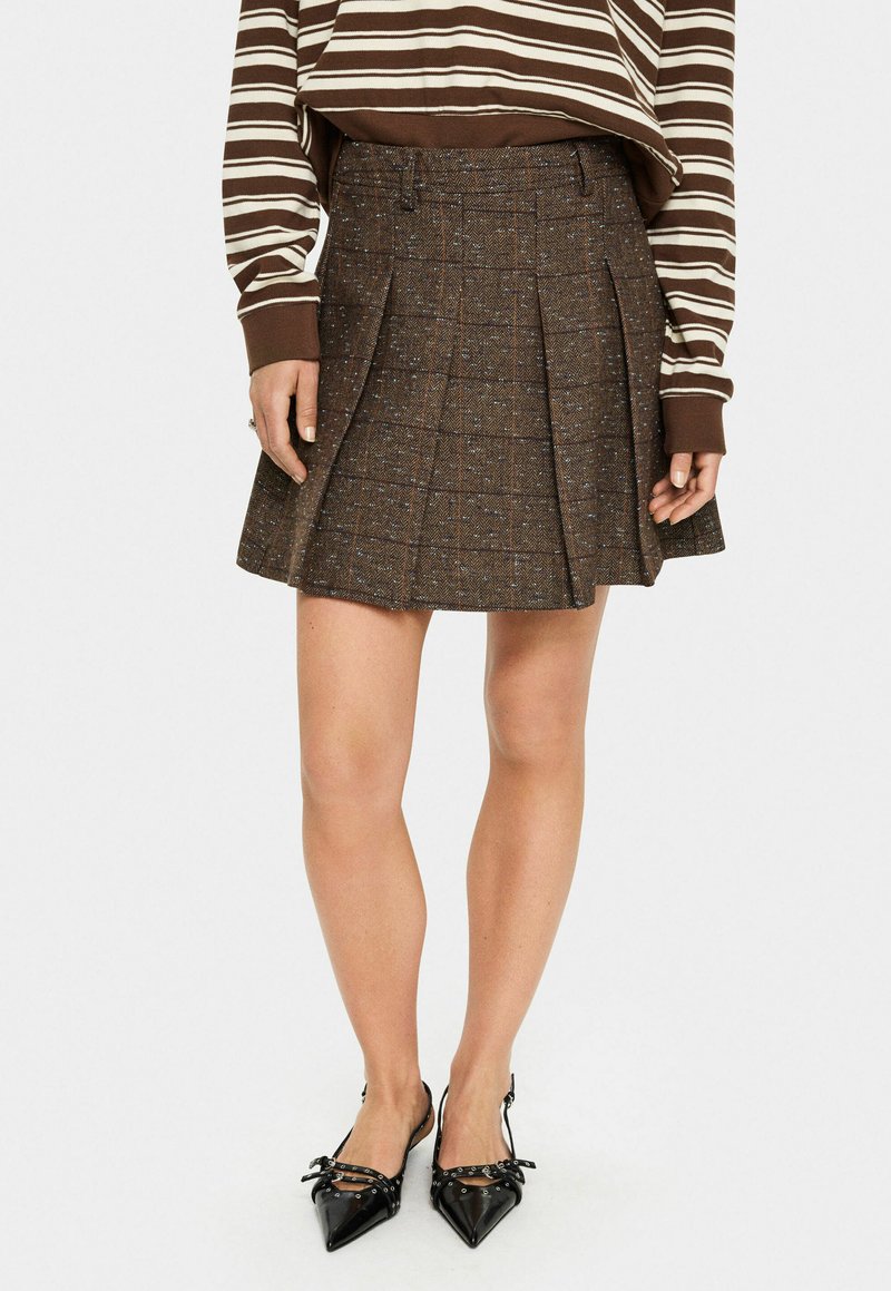 Brown tweed pleated skirt with a check pattern. Textured fabric with subtle blue specks. Paired with black pointy-toed shoes.