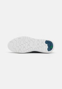 Suela de zapato con una base de goma blanca texturizada y un patrón de panal, acentuada por un detalle hexagonal verde en el talón.