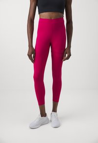 Fuchsiové legíny s vysokým pasem, hladkou texturou a blízkým střihem k tělu; zkombinované s bílými sportovními botami.