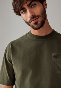 T-shirt verde oliva a maniche corte realizzato in tessuto morbido, con scollatura rotonda e taschino a sinistra sul petto.