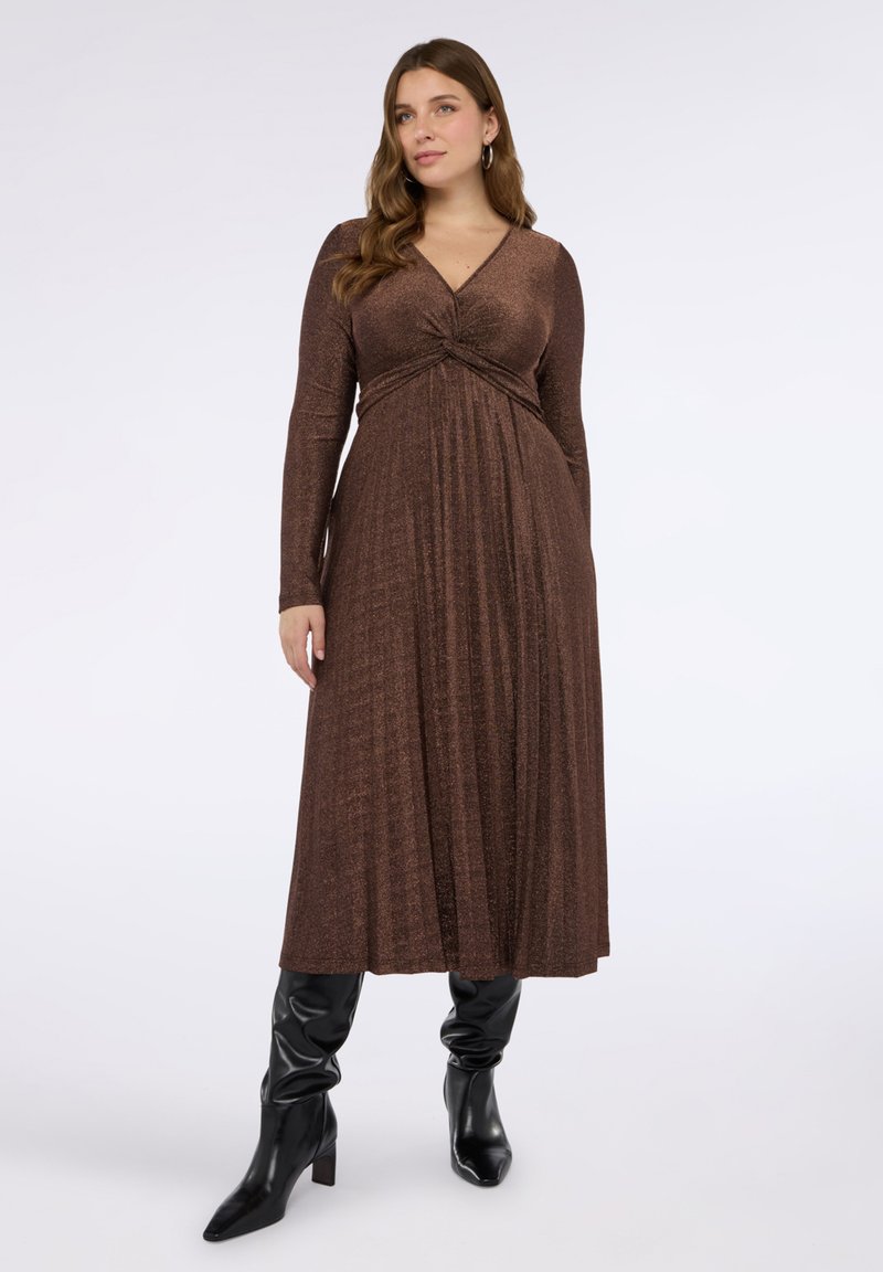 Brun klänning med lång ärm, V-ringning och knytdetalj i midjan, med en flödande kjol och texturerat tyg. Matchad med svarta knähöga stövlar.