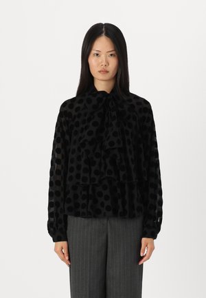 Black polka dot blouse with ruffled tiers, long sleeves, and a bow tie neck. Made from a sheer fabric with a smooth texture.
