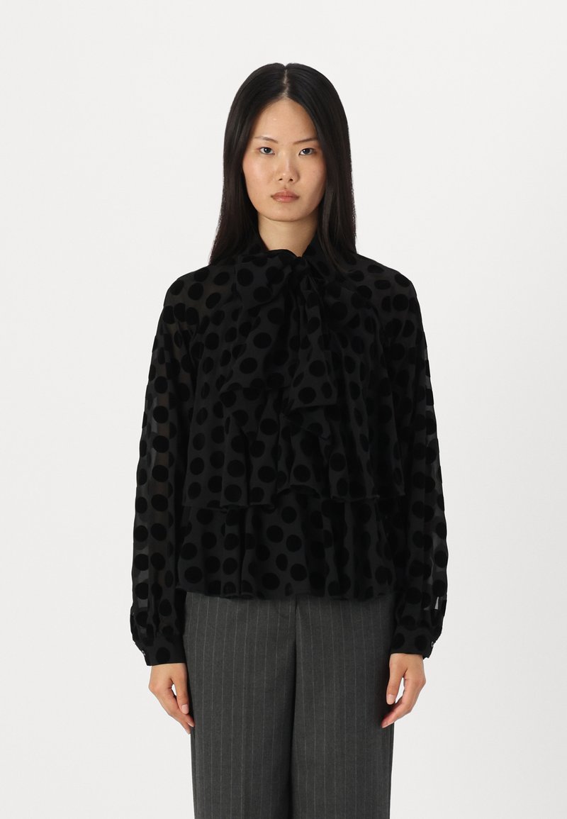 Black polka dot blouse with ruffled tiers, long sleeves, and a bow tie neck. Made from a sheer fabric with a smooth texture.