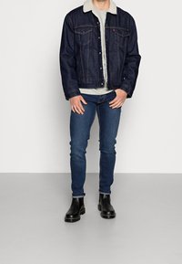 Mörk denimjacka med fårskinnskrage, grå stickad tröja under, i kombination med mörkblå slim fit jeans och svarta Chelsea-boots.