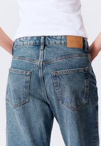 Jean en denim bleu clair à taille haute, dotés de deux poches arrière, de coutures contrastantes et d'une étiquette en cuir marron sur la ceinture.