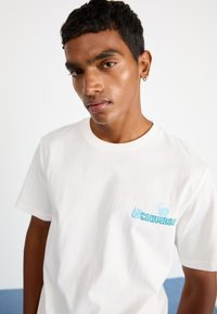 Hvit bomulls T-skjorte med lyseblå "Converse" trykk med designelementer, rund hals og korte ermer.