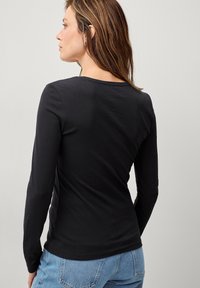 Sort langærmet skjorte med en tætsiddende design, glat tekstur og bred halsudskæring, parret med lyseblå højtaljede jeans.