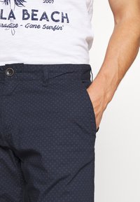 Shorts bleu marine en tissu à motif subtil, dotés d'un bouton à l'avant, de poches latérales et d'une coupe décontractée.