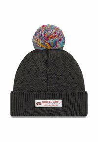 Berretto di lana nero con un pompon colorato sopra, con un'etichetta bianca con testo rosso che recita "CRUCIAL CATCH INTERCEPT CANCER" sul risvolto.
