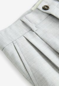 Pantaloni eleganti grigi chiari con un tessuto testurizzato, caratterizzati da pieghe frontali e chiusura con bottone. Vita ben strutturata con elementi di design sartoriale.