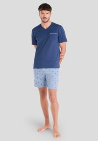 Camiseta navy de cuello en V con mangas cortas y un bolsillo en el pecho izquierdo, combinada con pantalones cortos azul claro con pequeños estampados de palmeras.