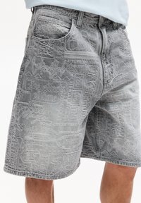 Shorts in denim grigio con un motivo testurizzato di varie frasi e disegni, con tasche tradizionali e una vestibilità dritta.