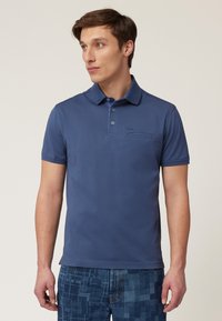 Blå polo skjorta med krage och två knappar. Kort ärm, tillverkad av slätt tyg. Har en fickdetalj med söm.