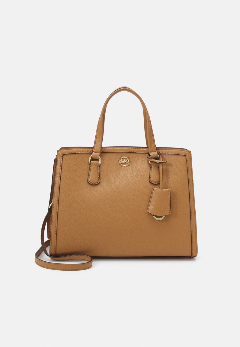 Sac à main en cuir fauve avec deux anses, bandoulière amovible et petit emblème doré sur le devant, posé sur un fond uni clair.
