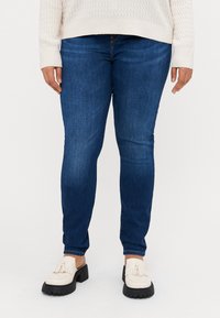 Skinny blue jeans made of denim, paired with cream loafers featuring fringe accents and a black platform. Sweater has textured pattern.